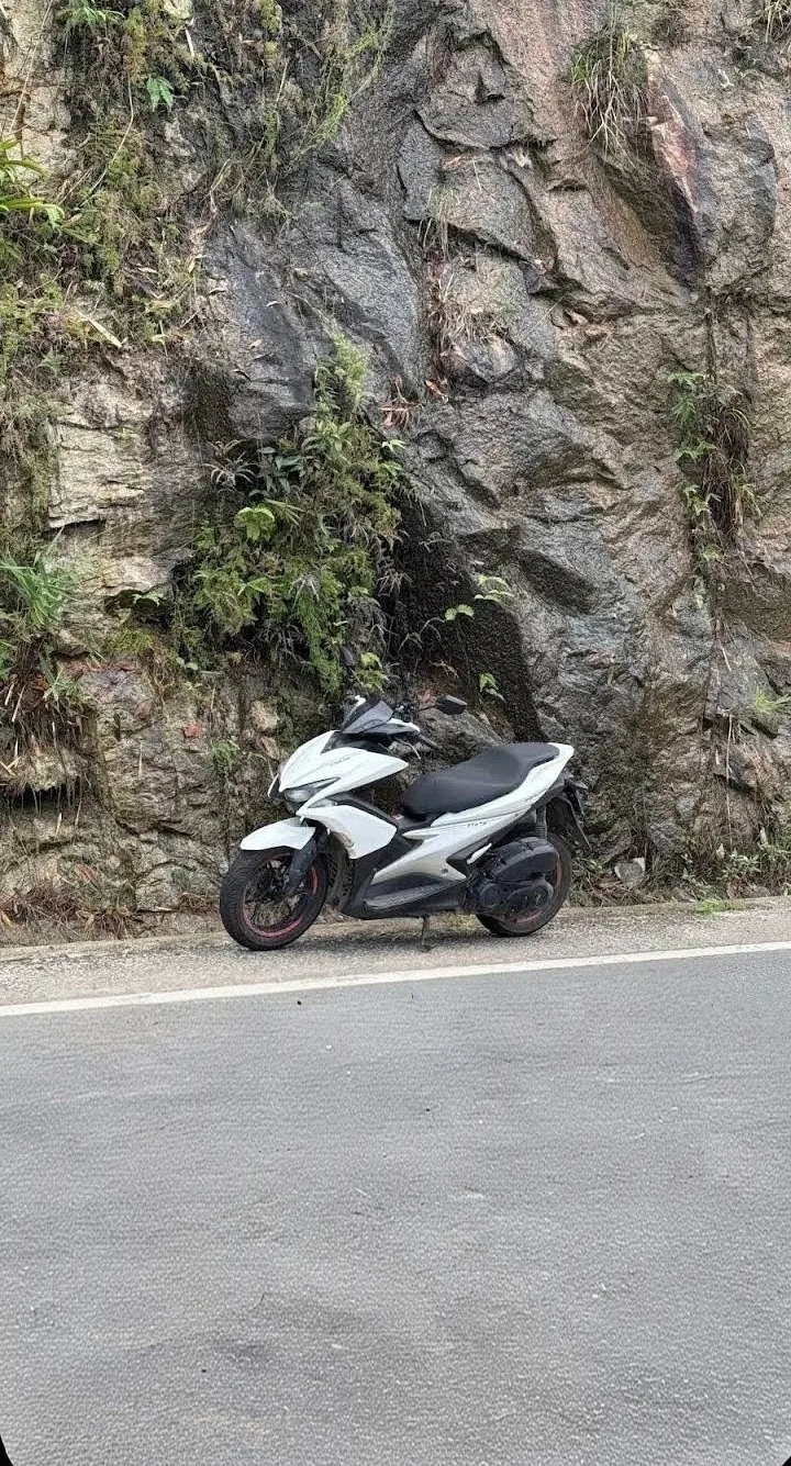 Белый Yamaha Aerox на горной дороге у скальной стены